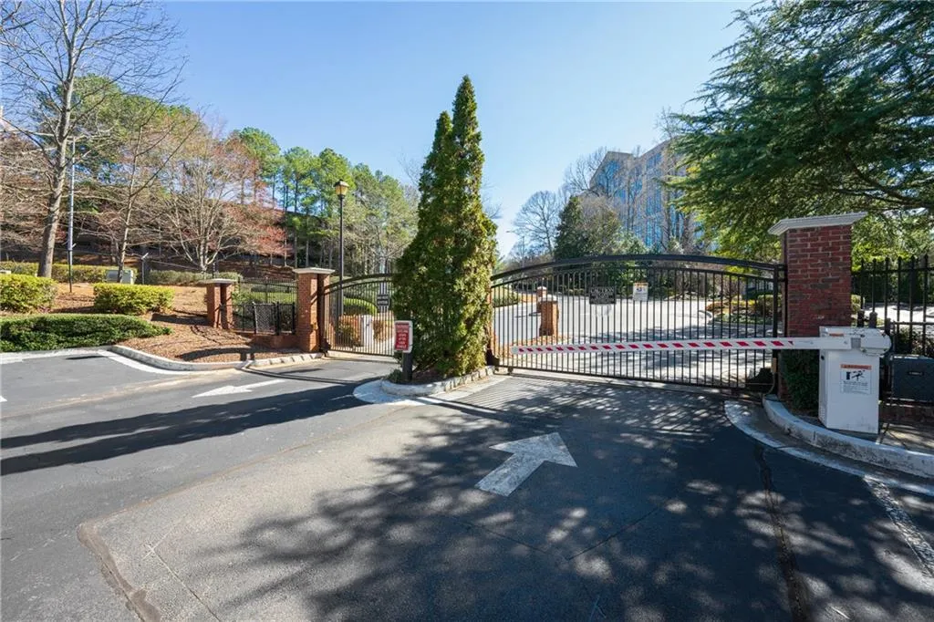 View of asphalt road featuring curbs, a gate, and street lighting