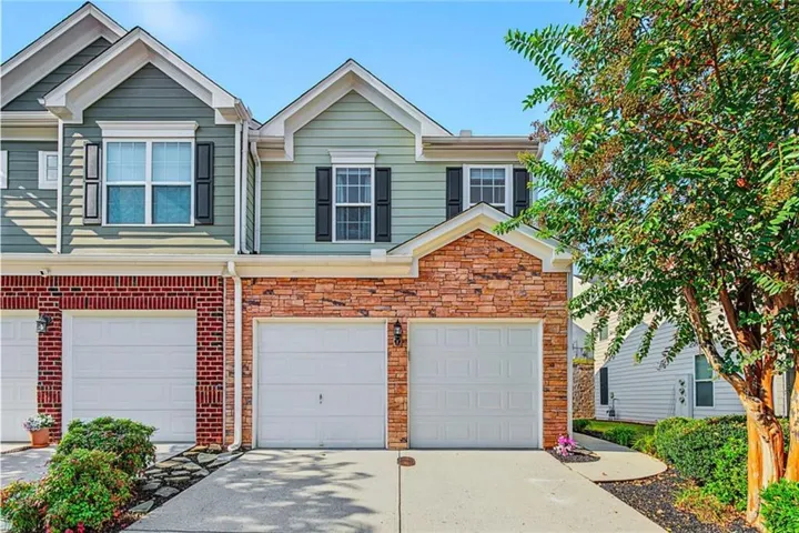 Two-car garage with individual doors, stone facade accents, decorative window shutters, and a paved driveway