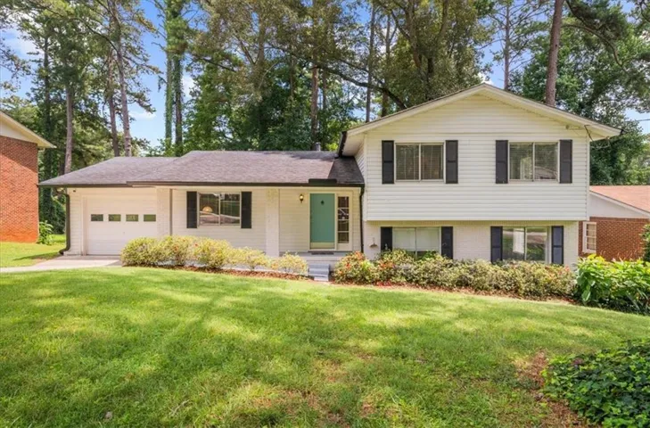 Split-level residence featuring white siding, black shutters, a two-car garage, and a teal front door
