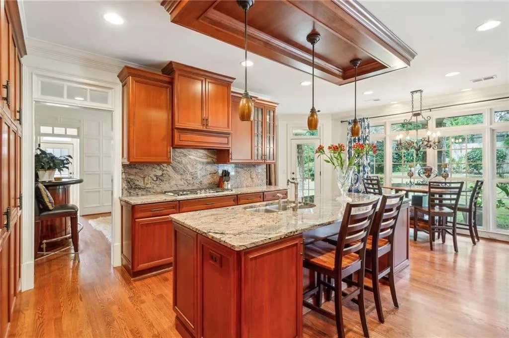 Kitchen with ornamental molding, brown cabinets, light stone counters, tasteful backsplash, and decorative light fixtures