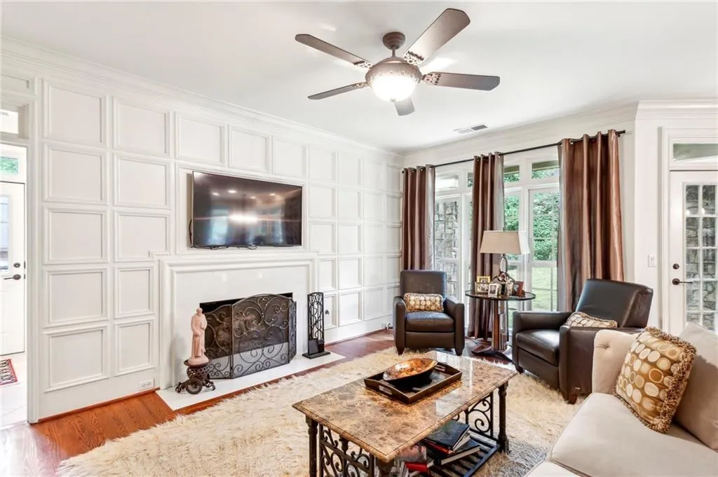 Living area with a fireplace with flush hearth, ornamental molding, light wood-style flooring, a ceiling fan, and a decorative wall