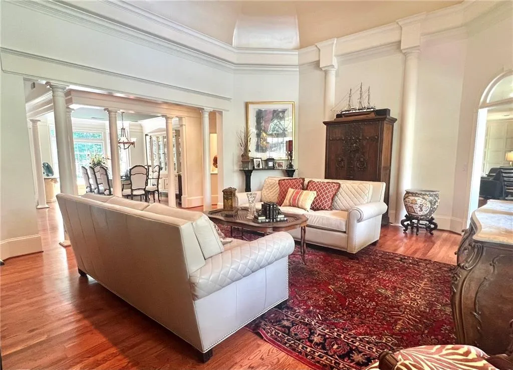 Living room with ornate columns, crown molding, wood finished floors, and a chandelier