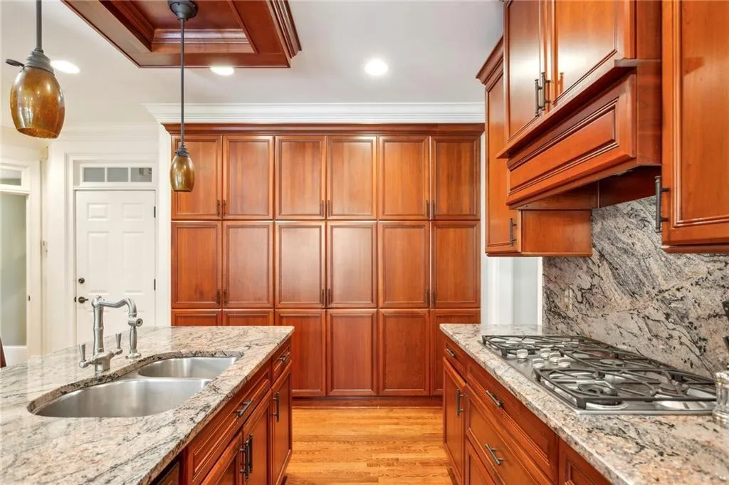 Kitchen featuring ornamental molding, pendant lighting, stainless steel gas stovetop, light wood-style floors, and brown cabinets