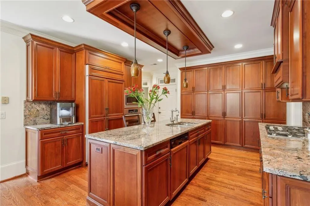 Kitchen with crown molding, decorative backsplash, light wood-style flooring, brown cabinetry, and light stone counters