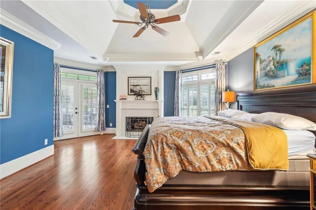Bedroom with ornamental molding, access to exterior, multiple windows, a large fireplace, and a raised ceiling