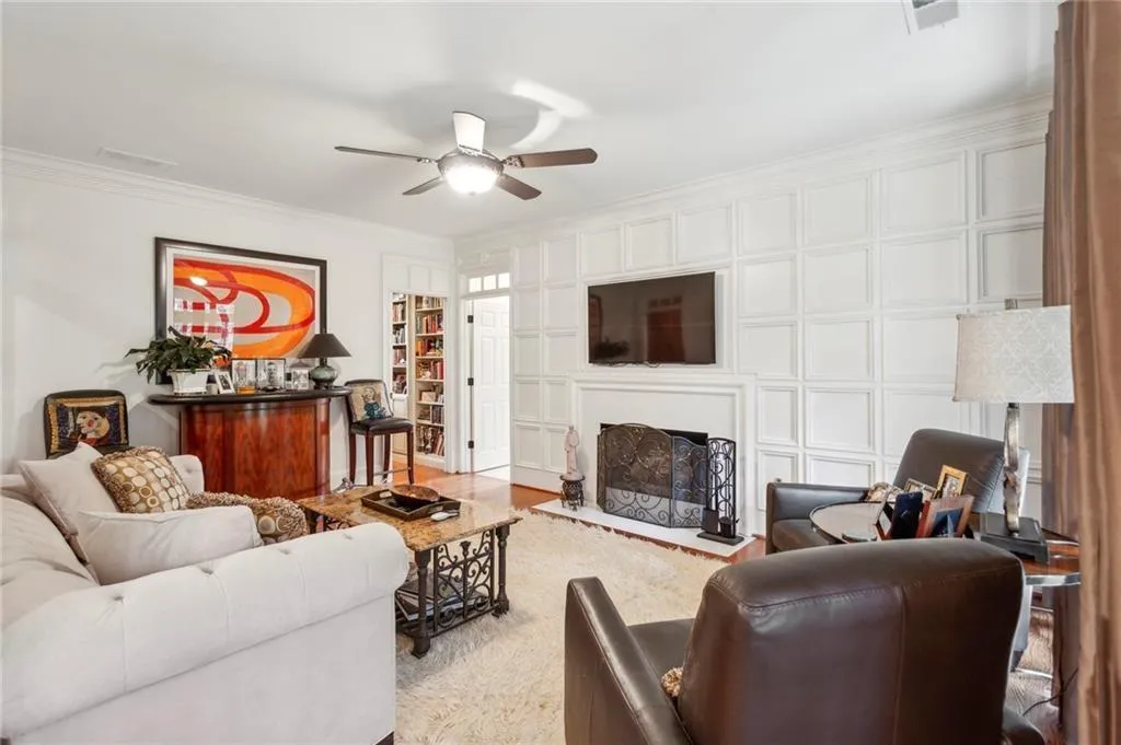 Living room featuring ornamental molding, ceiling fan, a fireplace with raised hearth, a decorative wall, and wood finished floors