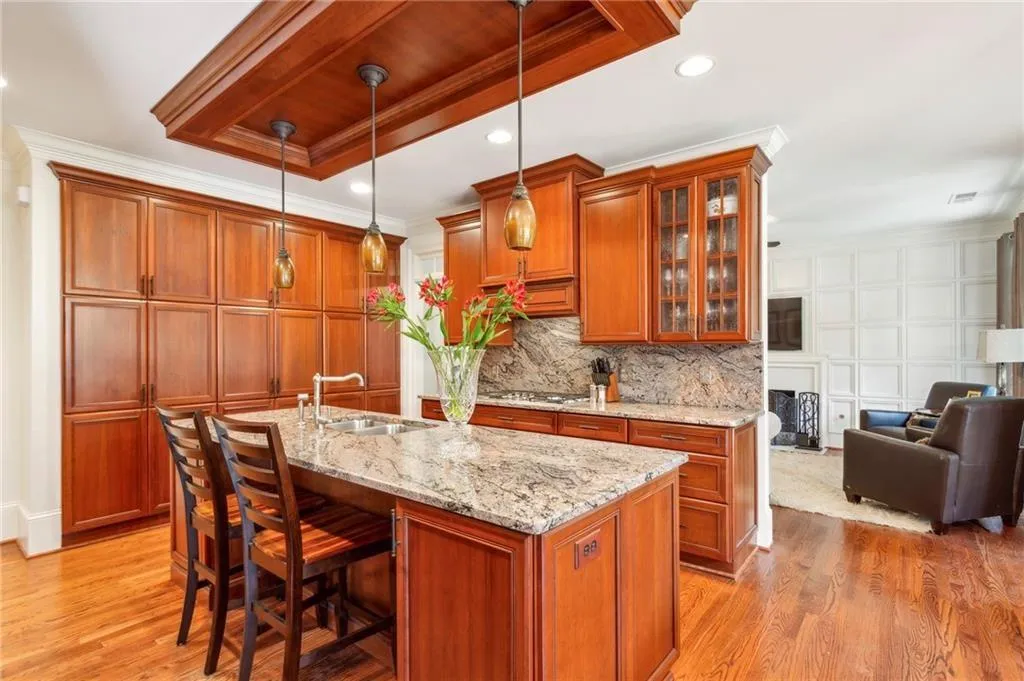 Kitchen with ornamental molding, glass insert cabinets, light wood-style floors, brown cabinets, and decorative light fixtures