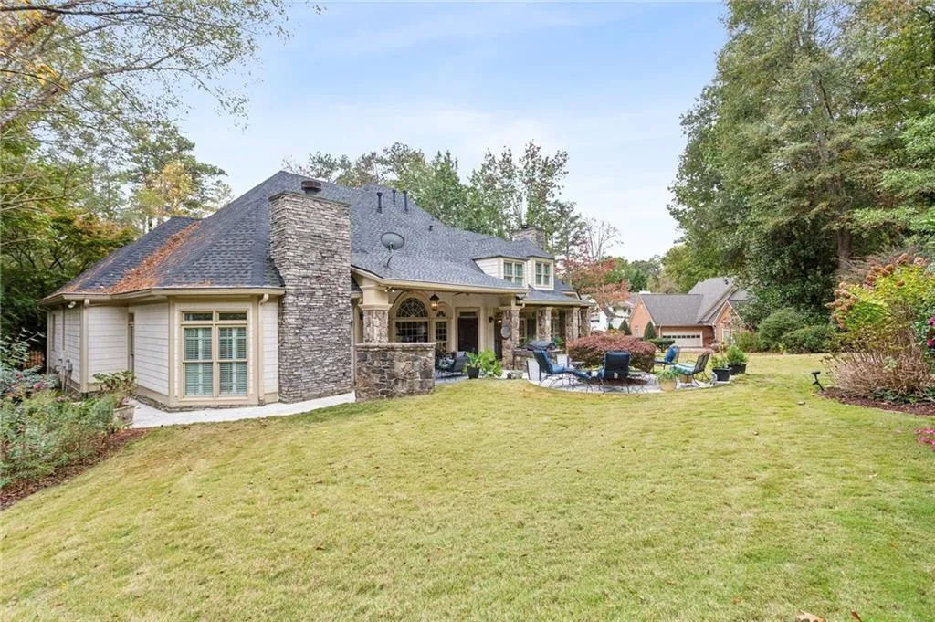 Back of house with a chimney, a patio area, stone siding, and a lawn
