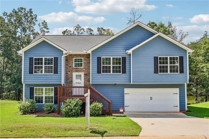 Split-level residence featuring blue siding, stone facade accents, a two-car garage, and a wood deck entry