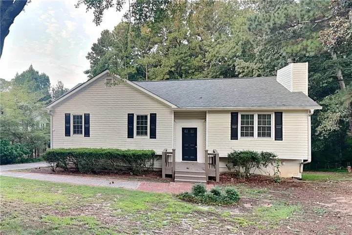Single-story residence featuring siding exterior, dark roof, dark paneled entry door, front porch with railings, and established perimeter landscaping