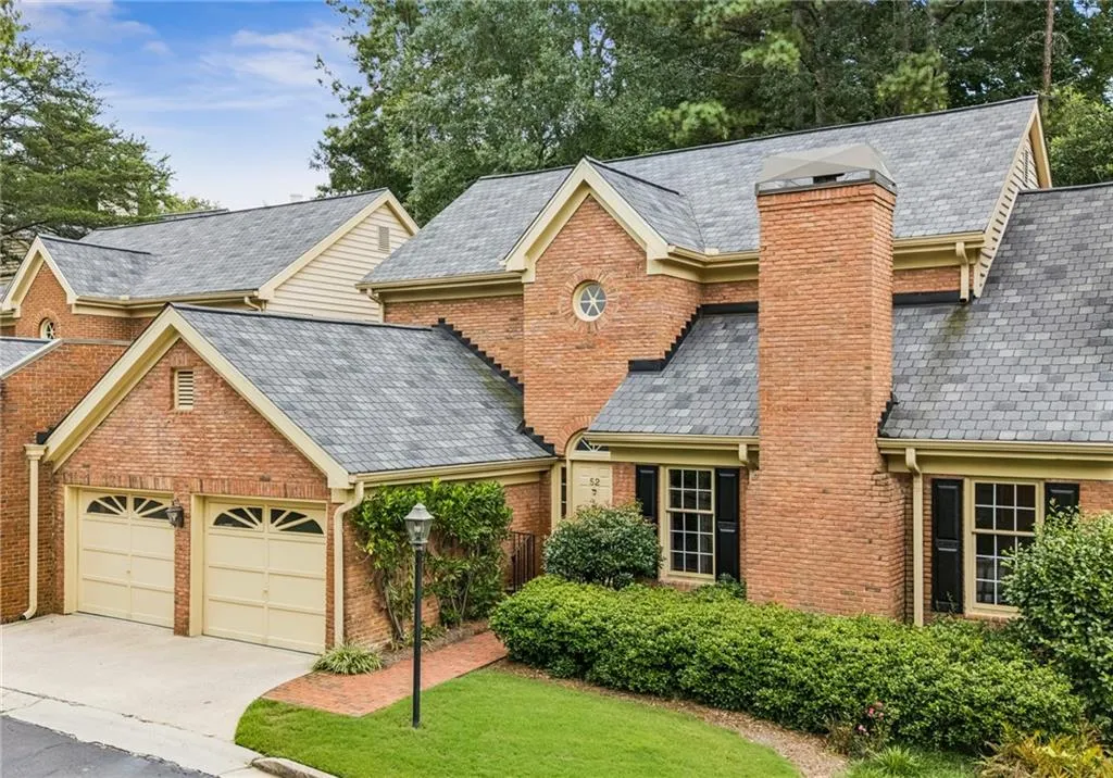 View of front of property featuring a chimney, brick siding, a front yard, and concrete driveway