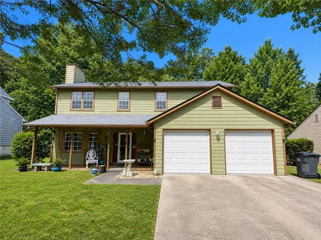 Two-story residence with a covered front porch, an attached two-car garage, light green siding, and a concrete driveway