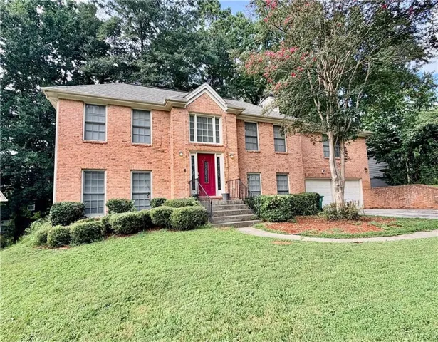 Brick exterior with multiple windows, a prominent red front door, and a two-car garage