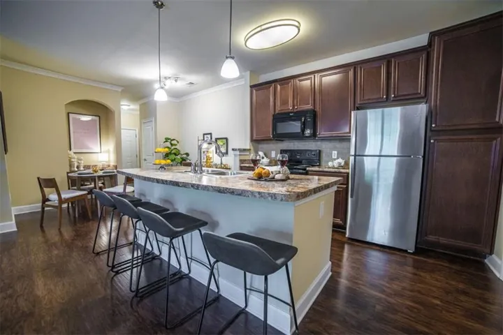 Kitchen with dark hardwood / wood-style floors, tasteful backsplash, stainless steel fridge, and an island with sink