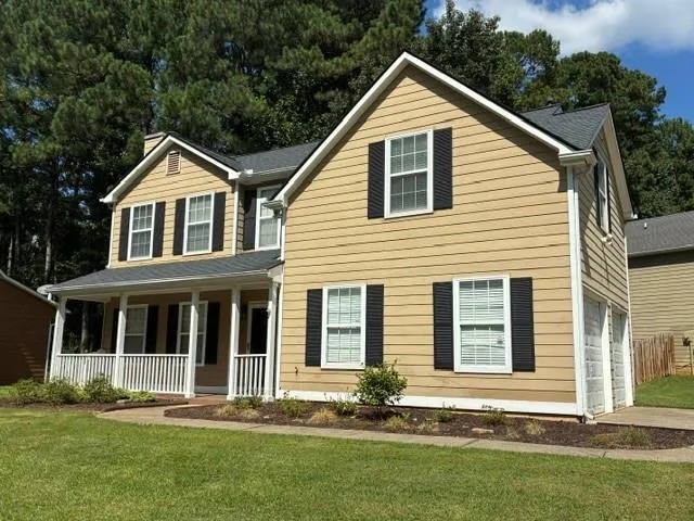 Two-story residence featuring a covered front porch, light-toned siding, dark window shutters, and an attached two-car garage