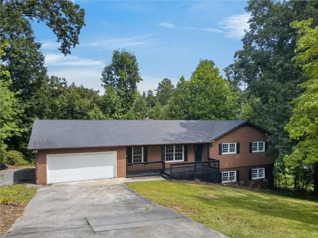 Split-level home featuring a two-car garage, brown siding, a dark roof, and a front deck with dark railings