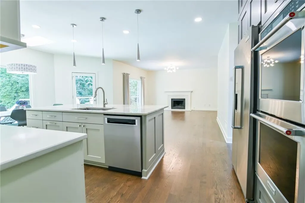 Kitchen with appliances with stainless steel finishes, dark hardwood / wood-style flooring, sink, pendant lighting, and a kitchen island with sink