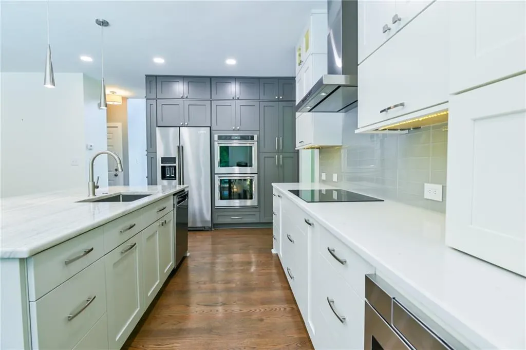 Kitchen with appliances with stainless steel finishes, dark hardwood / wood-style flooring, sink, wall chimney range hood, and pendant lighting