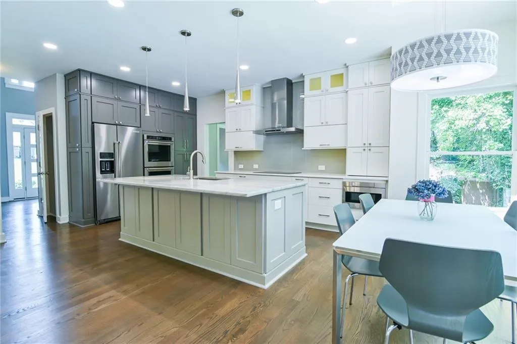 Kitchen featuring appliances with stainless steel finishes, dark hardwood / wood-style floors, wall chimney exhaust hood, an island with sink, and pendant lighting