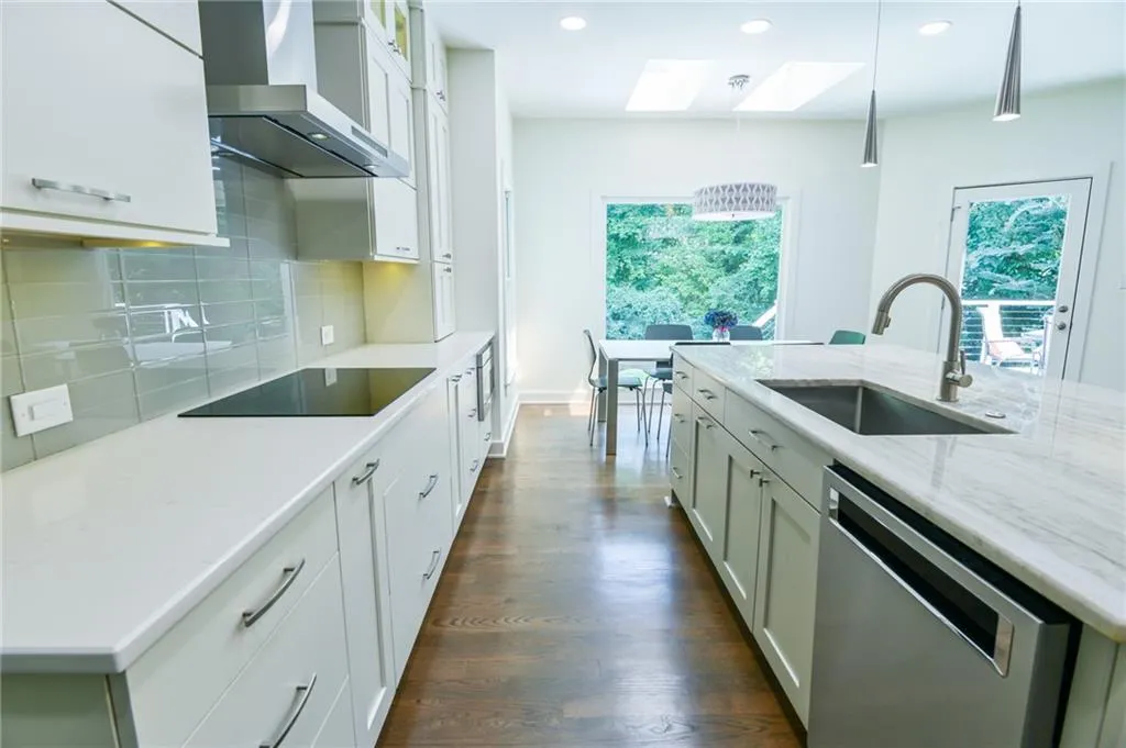 Kitchen featuring wall chimney exhaust hood, pendant lighting, stainless steel dishwasher, a skylight, and black electric cooktop