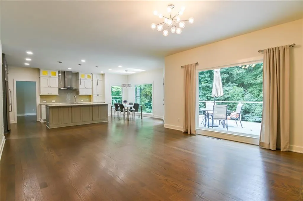 Kitchen featuring dark wood-type flooring, a notable chandelier, wall chimney range hood, and white cabinetry