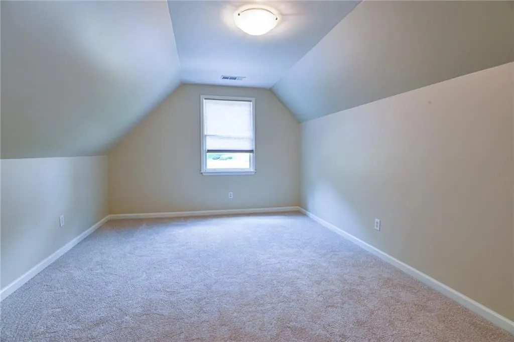 Bonus room with light carpet and vaulted ceiling