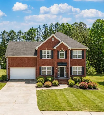 Brick facade home featuring a two-car garage, manicured lawn, established landscaping, arched window accents, and a paved driveway