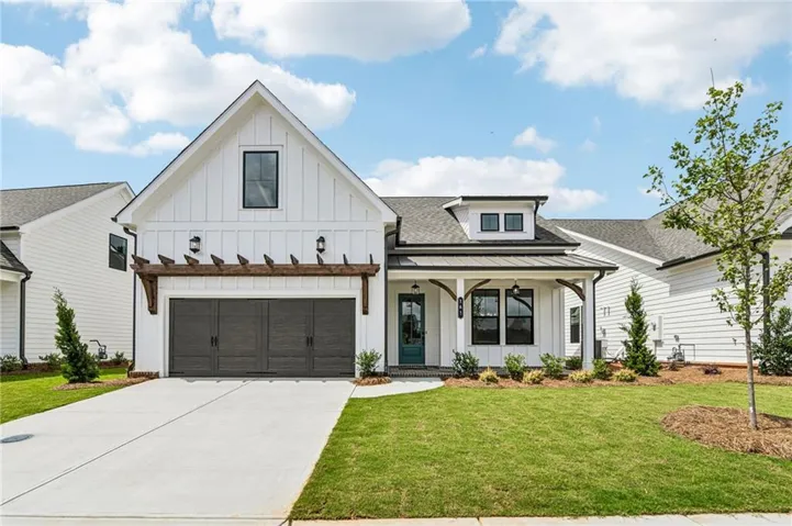 Modern farmhouse exterior featuring white board-and-batten siding, a dark gray garage door with decorative hardware, a covered front porch with exposed wood beams, a teal entry door, and a concrete driveway