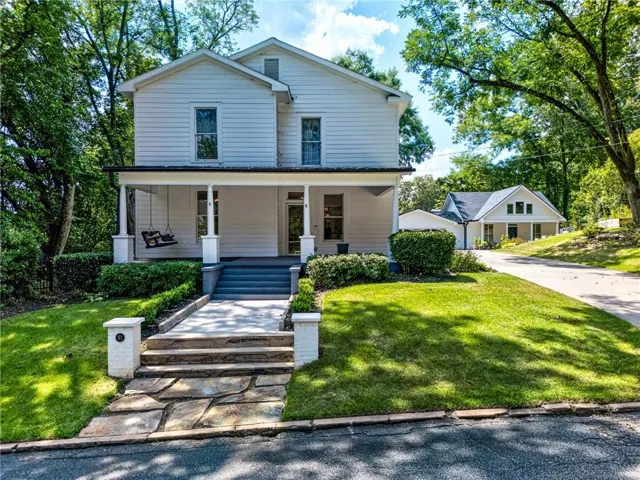 White siding exterior with a front porch, stone pathway, and mature trees