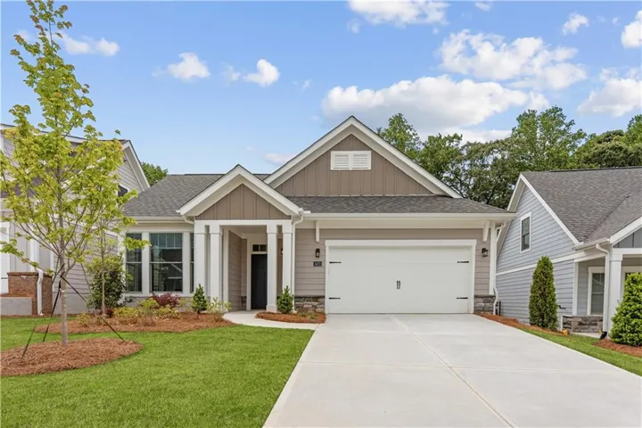 Craftsman-style home featuring a covered front entry with white columns, stone veneer accents, multi-pane windows, a two-car garage, and a concrete driveway