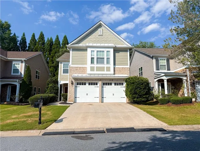 Two-story Colonial-style residence featuring a brick and siding exterior, peaked roofline with gable detailing, and a double-wide two-car garage