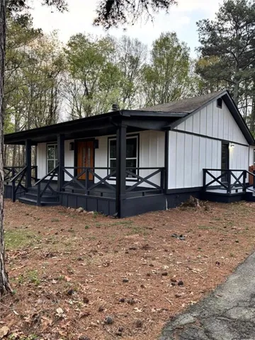 Board and batten siding with contrasting trim, a covered porch, wood plank front door, and dark exterior railings