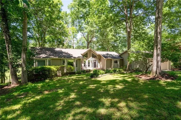 Siding exterior with multiple windows, surrounded by mature trees and a sloped lawn