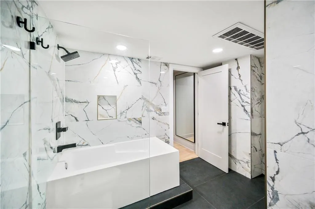 Bathroom featuring a glass-enclosed soaking tub, large-format stone-patterned wall tile, matte black fixtures, and dark-toned floor tile