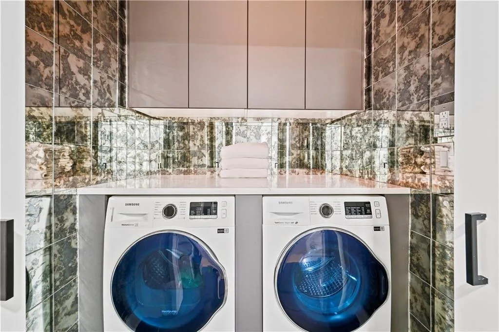 Custom laundry space featuring high-gloss cabinetry, white solid-surface countertop, antique-style mirrored tile backsplash, and built-in front-load appliances