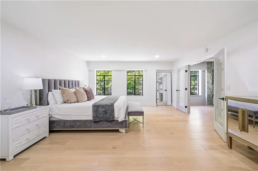 Spacious room featuring light-toned wood-finish flooring, recessed lighting, expansive multi-pane windows with black frames, and double glass-pane doors