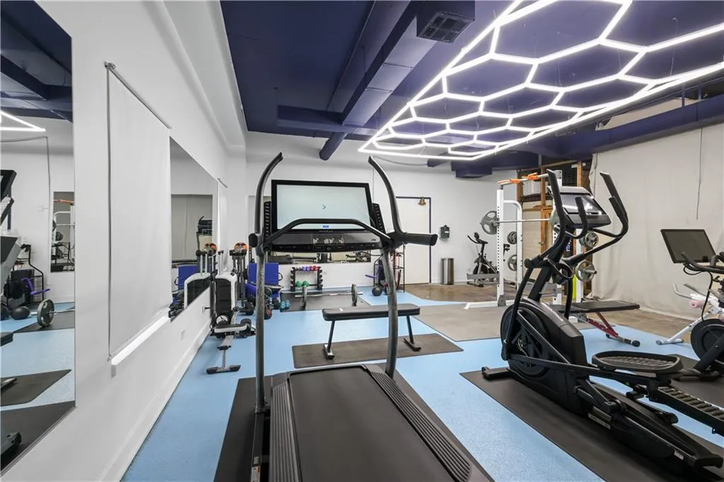 Fitness area featuring a hexagonal LED light fixture, blue rubberized flooring, and expansive wall-to-wall mirrors