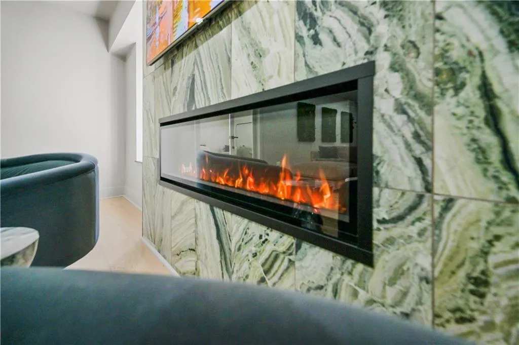 Linear electric fireplace featuring a black metal surround set into a floor-to-ceiling accent wall clad in large-format green veined stone tile