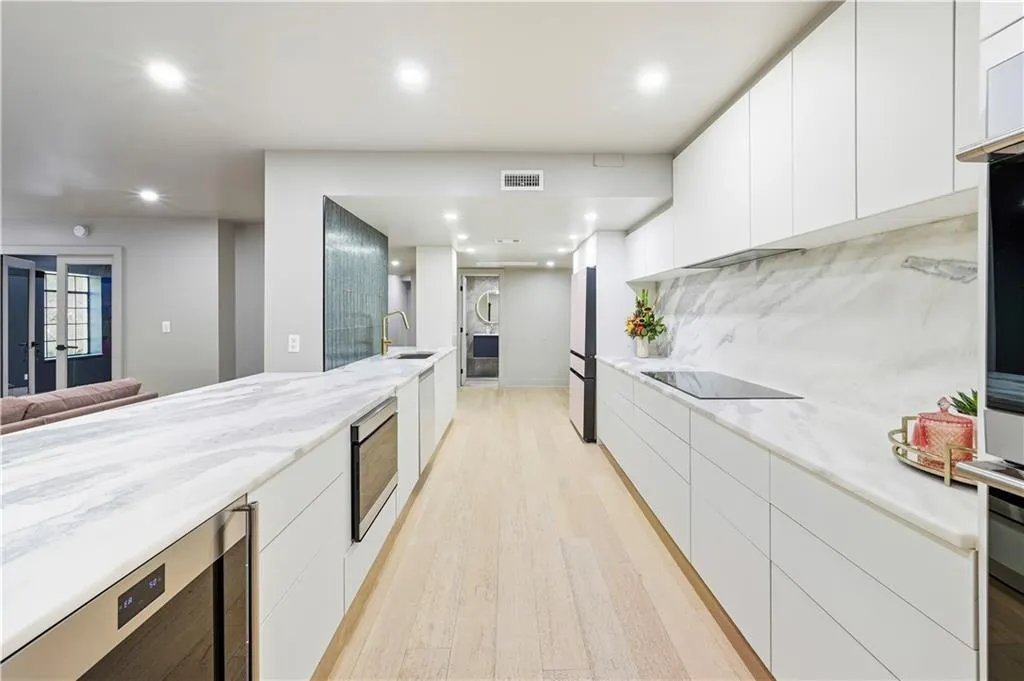 Kitchen featuring white slab-front cabinetry, stone-finish countertops with matching full-height backsplash, wood-finish flooring, built-in stainless steel appliances, and recessed lighting