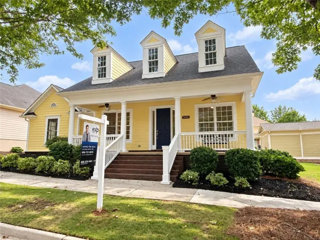Yellow exterior with multiple dormer windows, a covered front porch, white railings, and mature landscaping