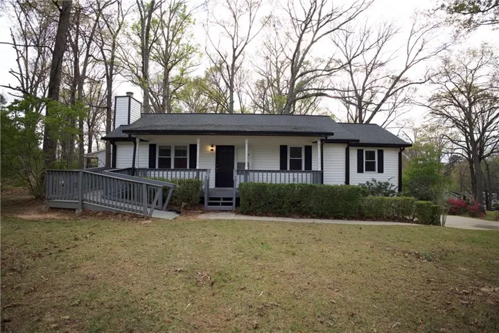Single story home featuring covered porch, a chimney, and a front yard