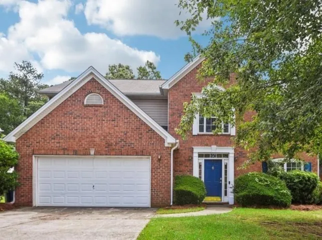 Brick facade residence with a two-car garage, prominent blue entry door, white window shutters, and manicured shrubbery