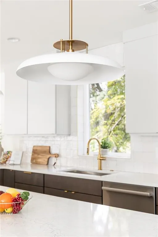 Kitchen featuring white cabinetry, backsplash, stainless steel dishwasher, dark brown cabinets, and light stone countertops