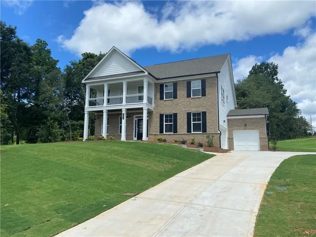 Two-story residence featuring a brick and siding exterior, a prominent two-tier front porch with white columns, black framed windows with shutters, an attached garage, and a concrete driveway