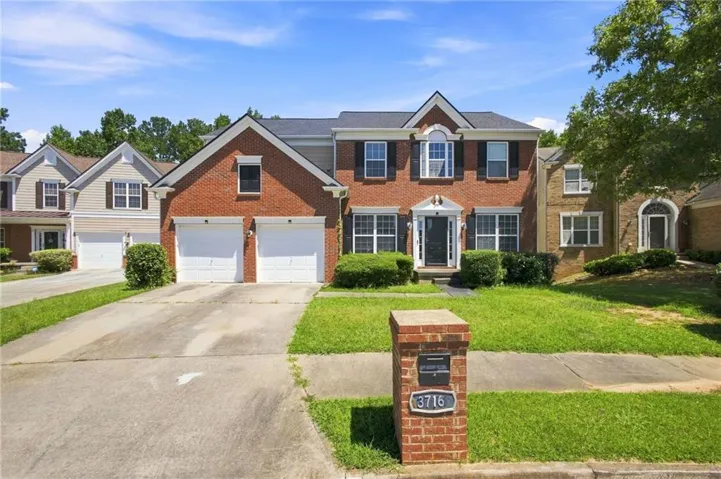 Brick Colonial with two-car attached garage, manicured front lawn, and mature landscaping