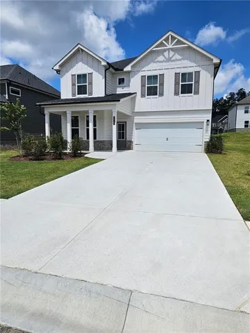 White exterior with dark shutters, covered front entry, two-car garage, concrete driveway, and a shingled roof