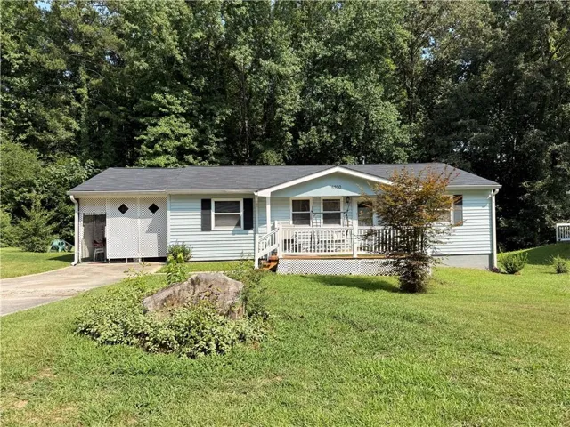 Light blue siding residence featuring a covered front porch with white railings, a dark shingle roof, and a paved driveway