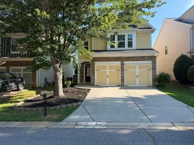 Two-story residence featuring yellow siding, a stone facade, and a two-car garage with light-colored doors