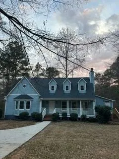 New england style home featuring a porch, a chimney, and a front lawn