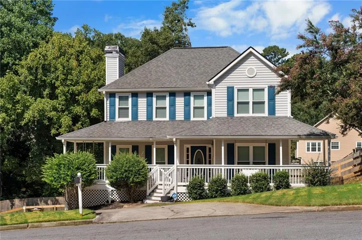 Two-story residence featuring light gray siding with blue shutters, a full-width covered front porch, and a shingled roof